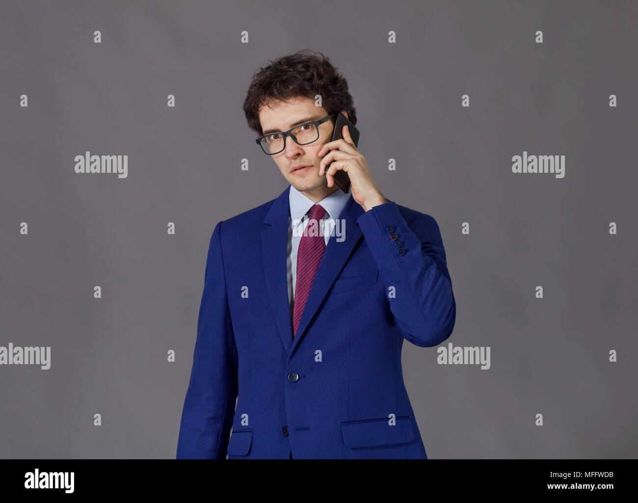 Curly capo-uomo che indossa in giacca blu e bicchieri parla al telefono cellulare Foto Stock