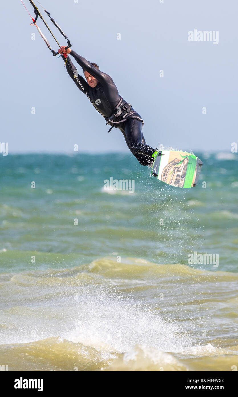 Uomo di eseguire uno stunt mentre kitesurf in mare, volare in aria. Visualizzazione verticale. Foto Stock