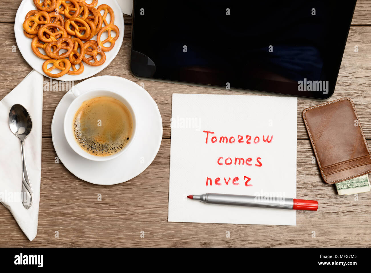 Tovagliolo proverbio del messaggio sul tavolo di legno con caffè, alcuni alimenti e tablet PC domani arriva mai Foto Stock