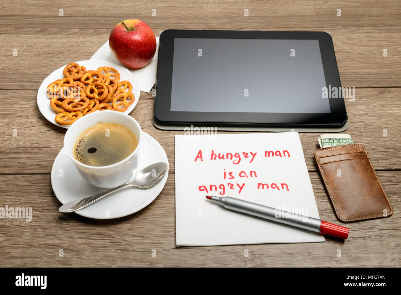 Tovagliolo scrittura proverbio del messaggio sul tavolo di legno con caffè, alcuni alimenti e tablet PC un uomo affamato è un uomo arrabbiato Foto Stock