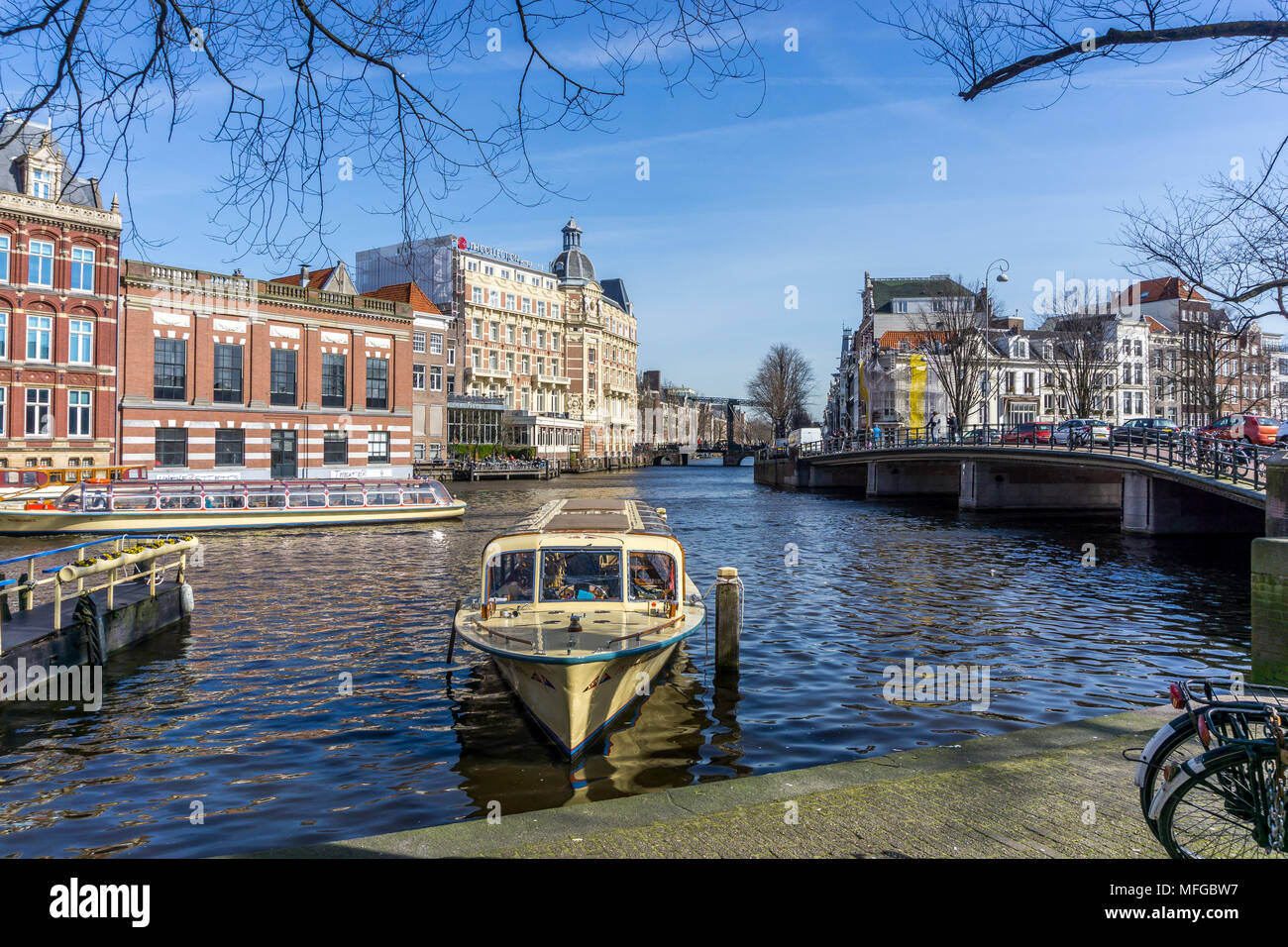 Barche sul fiume Amstel di Amsterdam, Paesi Bassi, Europa con NH Doelen Amsterdam Hotel raccolta nel backdround. Foto Stock