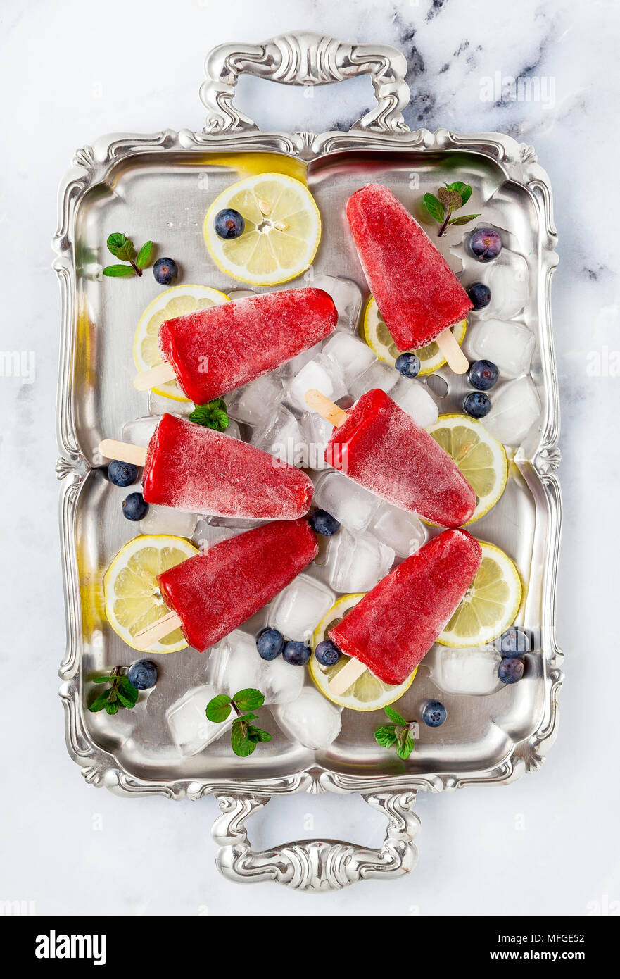 Congelati succo di fragola snack ice pop o ghiaccioli su un bianco tavola di marmo con mirtilli e il ghiaccio con la menta. estate gelati freschi sfondo alimentare Foto Stock