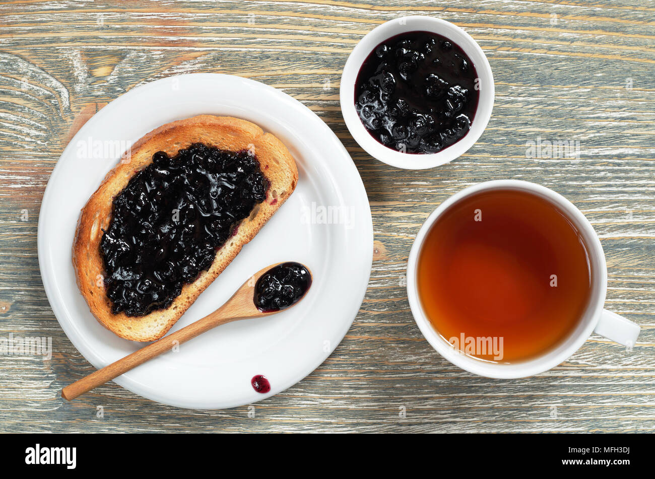 Tazza di tè e deliziosi toast con marmellata di mirtilli per la colazione su un vecchio tavolo di legno, vista dall'alto Foto Stock