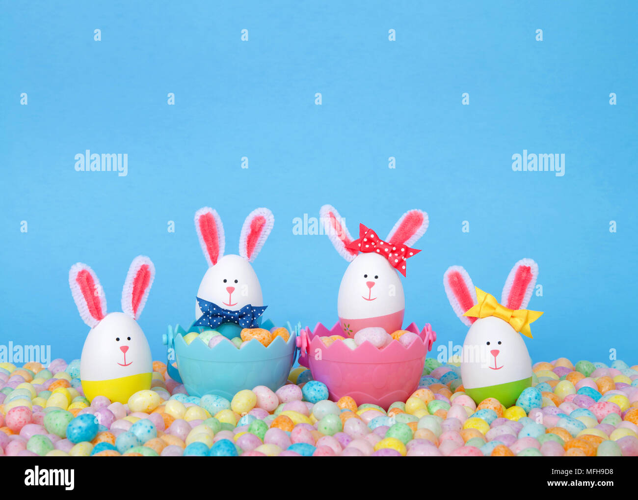 Craft conigli pasquali realizzati da uova in plastica in due cesti pieni di caramelle con due piedi in pastello Jelly Beans con un fondo di colore azzurro. Divertimento EAS Foto Stock