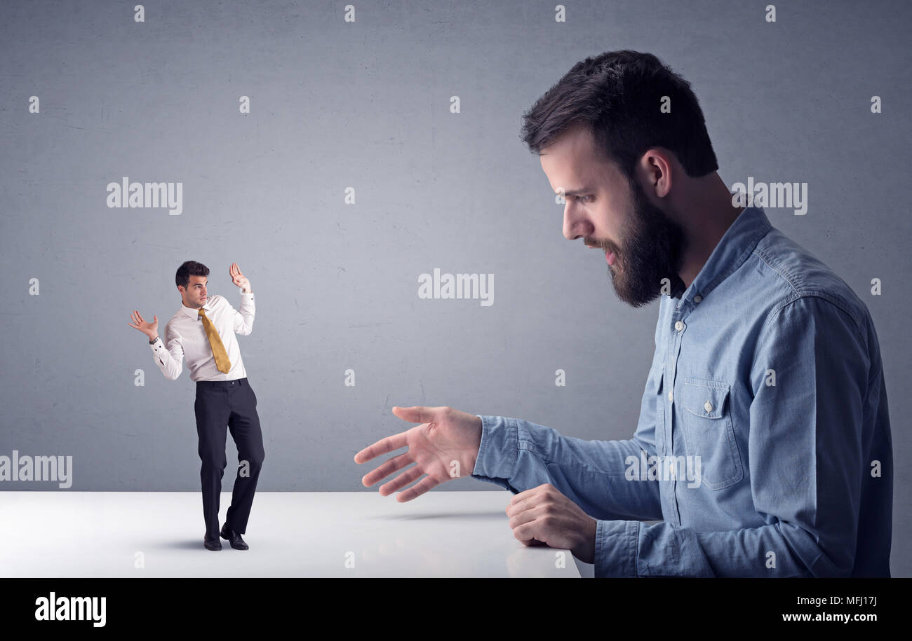Giovane imprenditore professionale essendo arrabbiato con un altro imprenditore in miniatura di fronte a uno sfondo grigio Foto Stock