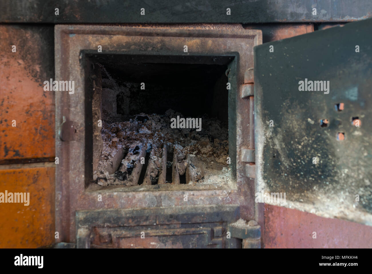 Stufa rurale con sportello aperto. Sacco di ceneri e carbone visibile all'interno della stufa Foto Stock