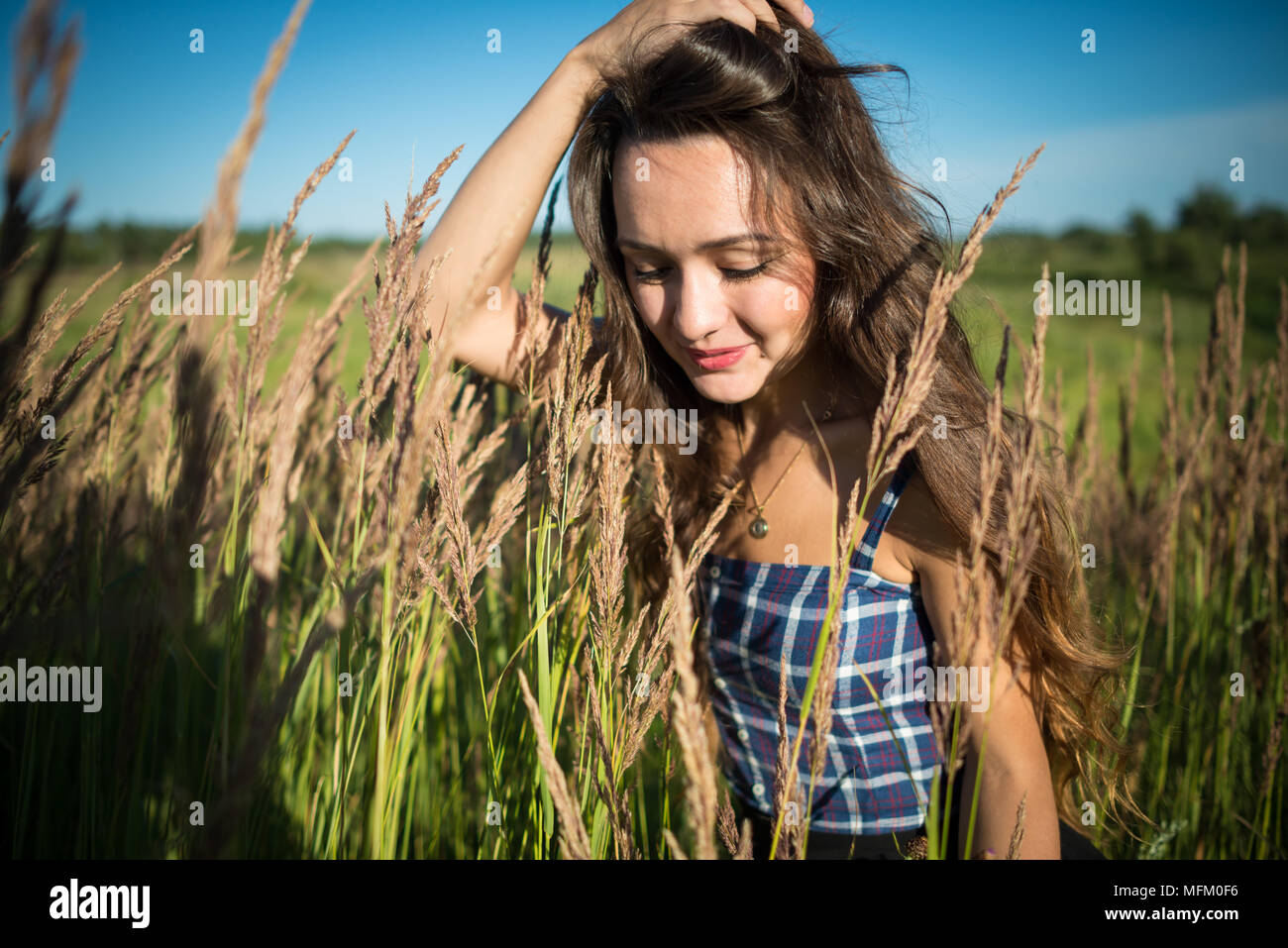 Giovane donna in piedi su un campo di erba nel giorno d'estate. Bella ragazza è la correzione di acconciatura sullo sfondo della natura. Foto Stock