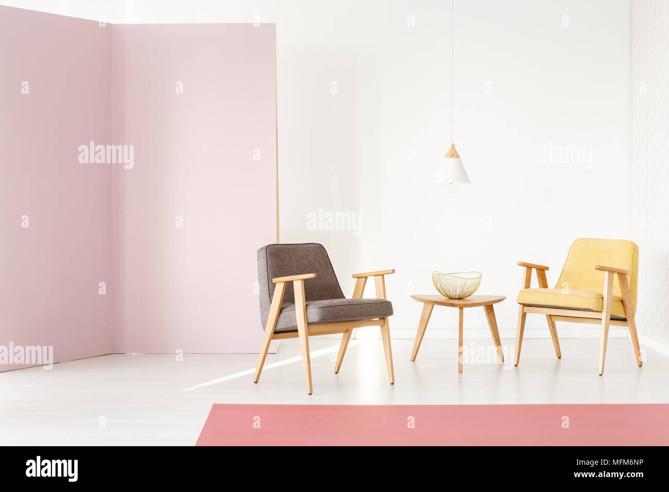 Raggi di sole che splende su una moderna, poltroncina in legno in un elegante colore rosa pastello interno con pareti bianche - disposizione dei mobili per una brochure Foto Stock