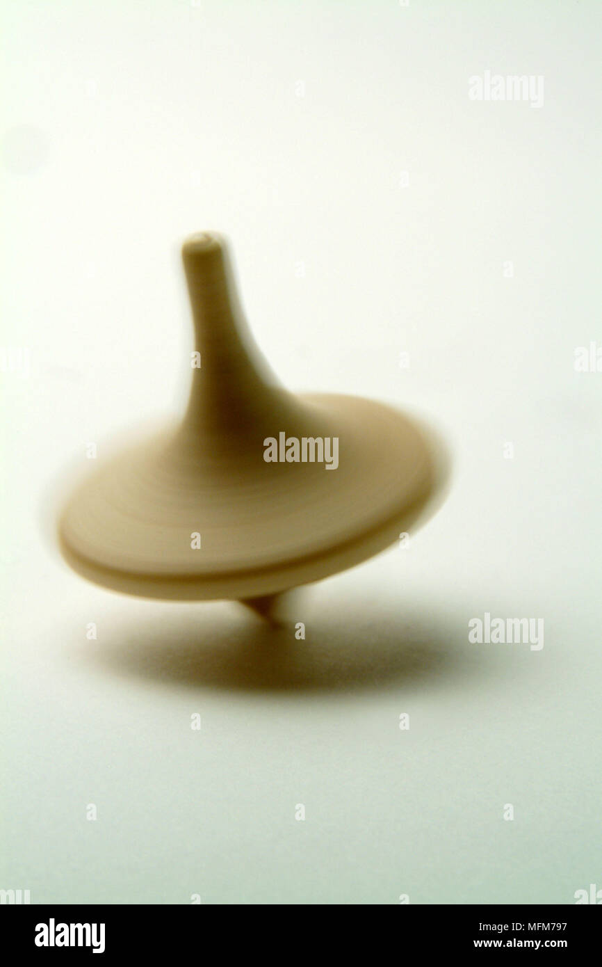 Un bambino piccolo e semplice in legno tradizionali top gira ad alta velocità producendo un blurr come esso si intreccia gyrateing attraverso il fondo del bianco Bilanciamento su di esso Foto Stock