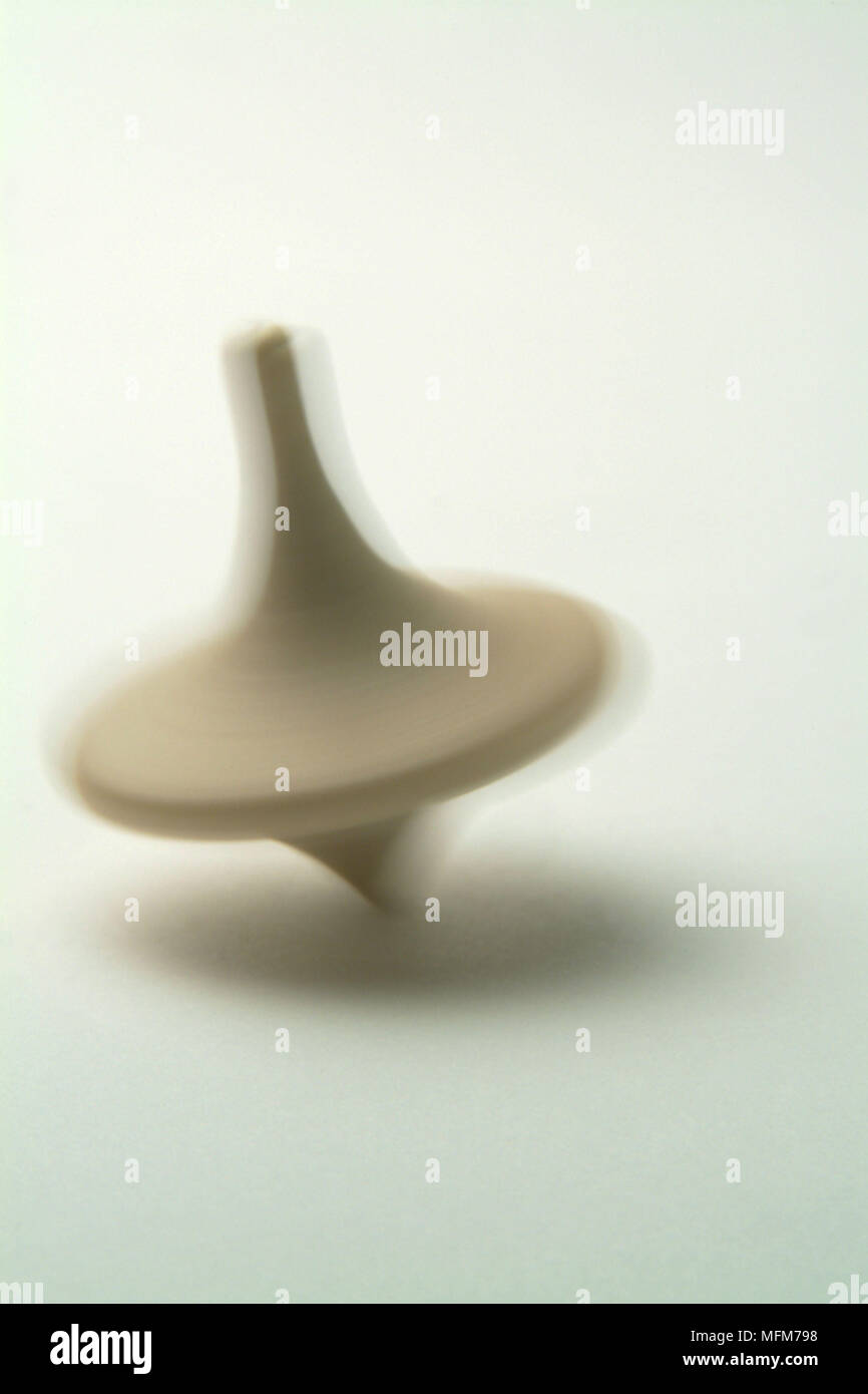 Un bambino piccolo e semplice in legno tradizionali top gira ad alta velocità producendo un blurr come esso si intreccia gyrateing attraverso il fondo del bianco Bilanciamento su di esso Foto Stock