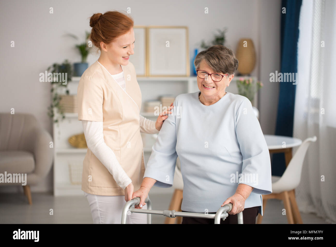 Professional medical custode in uniforme contribuendo sorridente donna senior con un walker in un soggiorno di lusso privata clinica sanitaria Foto Stock