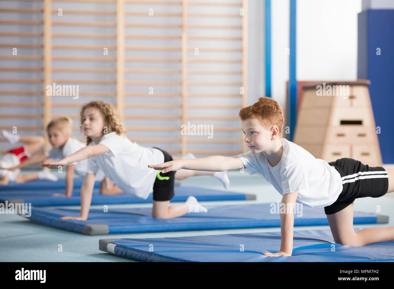 Gruppo di bambini facendo ginnastica su tappeti di blu durante l'educazione fisica classe a scuola Foto Stock