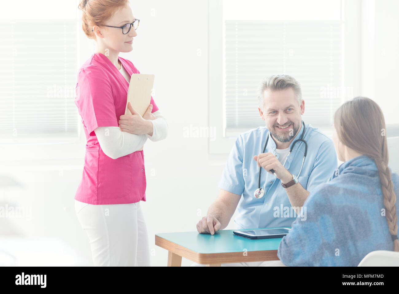 Doctor's assistant in uniforme rosa accanto a un medico di medicina generale durante il colloquio medico Foto Stock