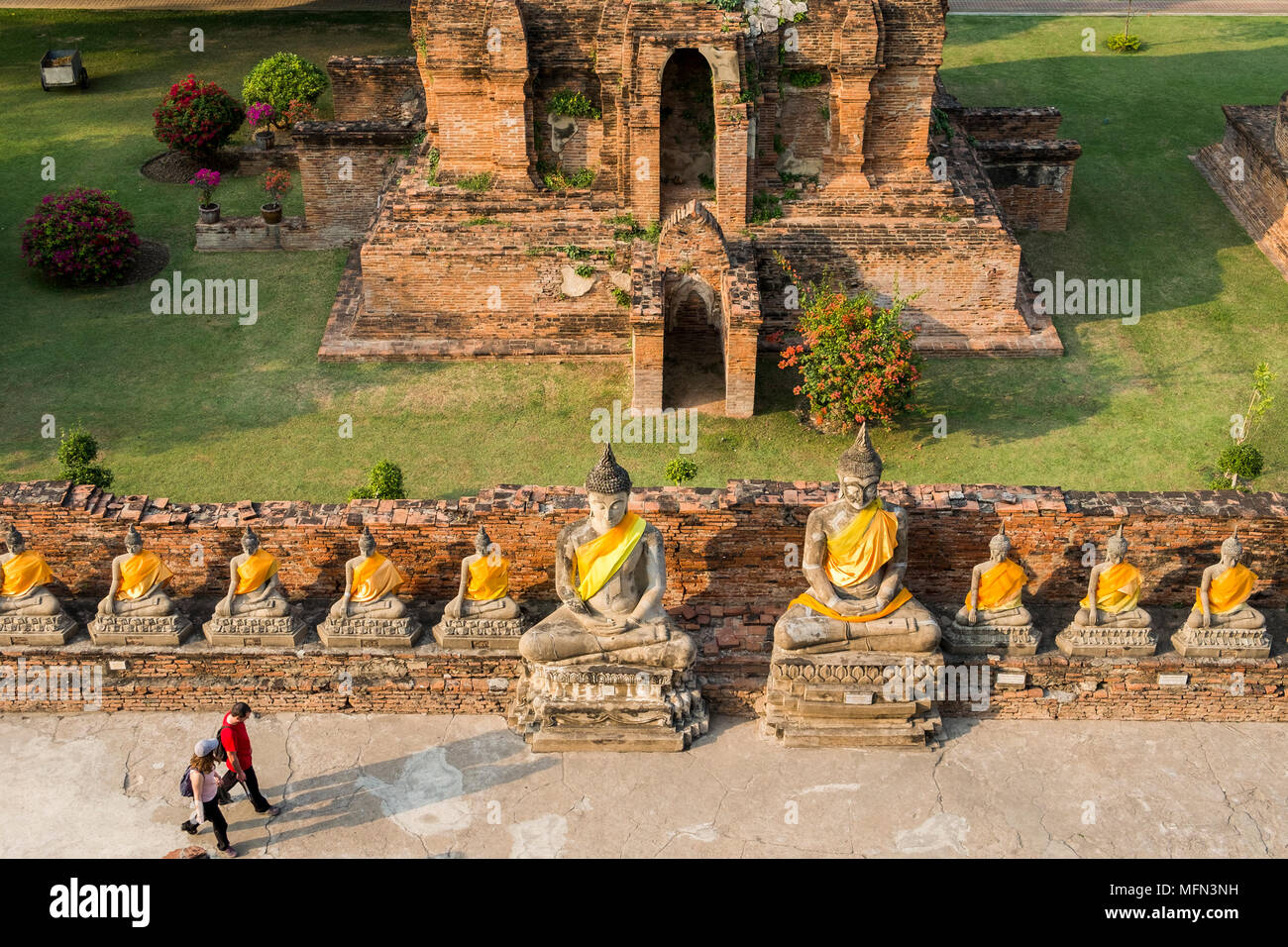 Due i visitatori a piedi passato una fila di statue di Buddha di Wat Yai Chai Mongkhon, un palazzo del XIV secolo tempio buddista, Ayutthaya, Thailandia. Foto Stock