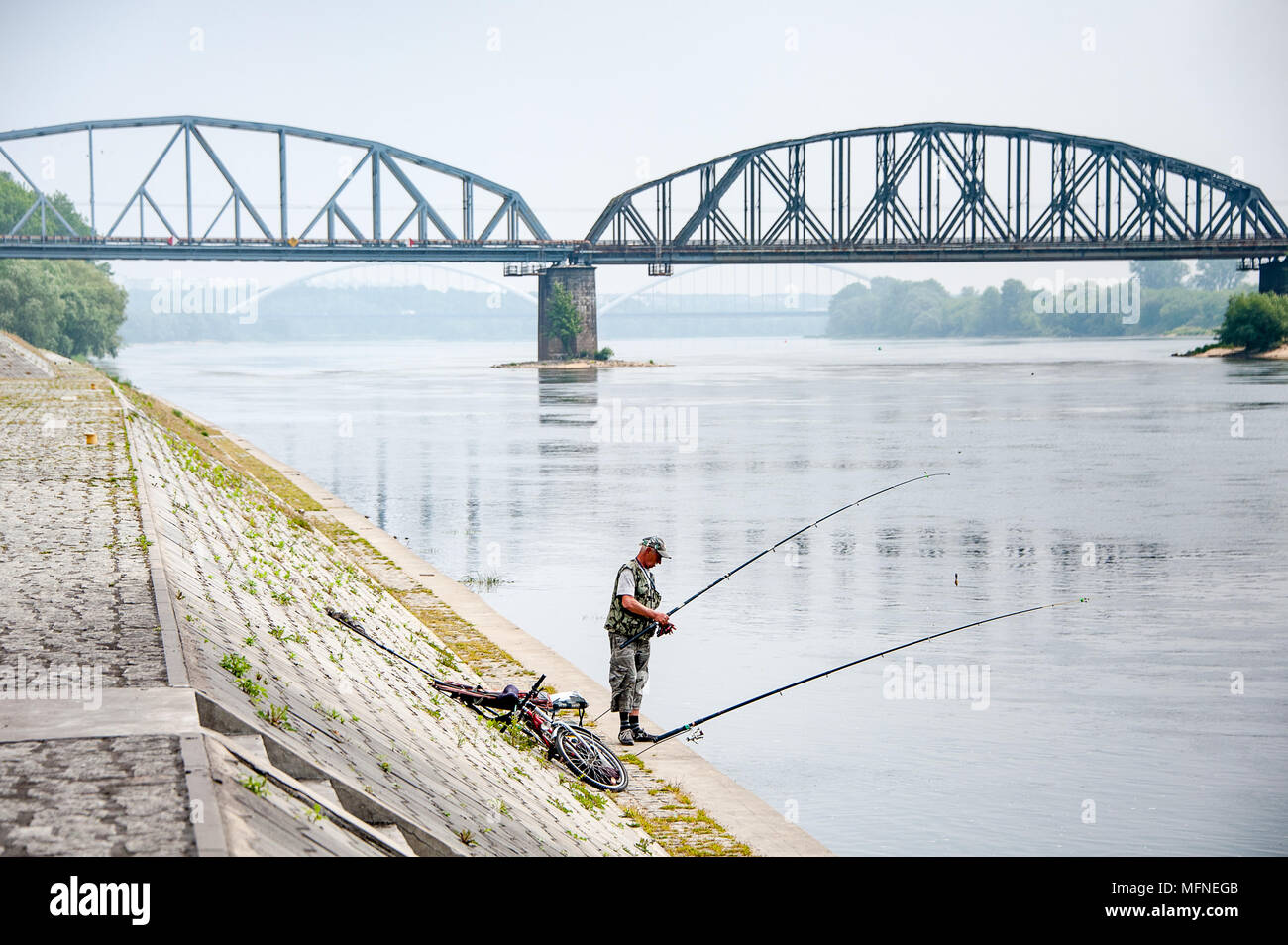 Uomo pesci sulle rive del fiume Vistola a Torun, Polonia. Brumoso paesaggio con la Josef Pilsudski ponte in background Foto Stock