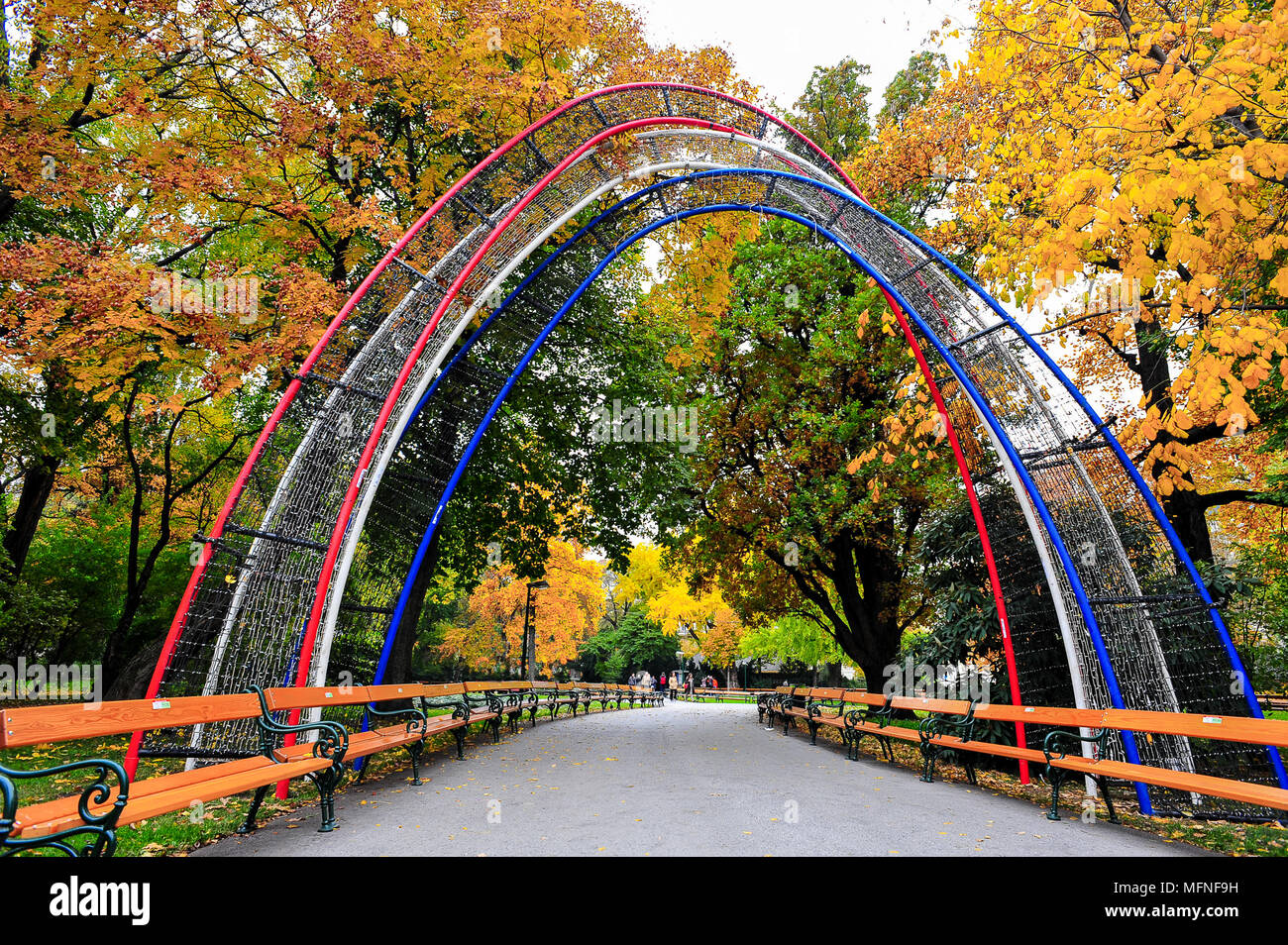 Il rosso e il blu ingresso ad arco, una colorata orlate da alberi avenue, e lunghi filari di panchine. In autunno, Stadtpark Vienna. Foto Stock
