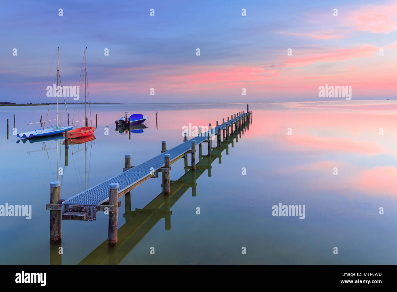 Una calma e tranquilla serata estiva in un lago con un pontile e barche a vela e un bellissimo cielo in background Foto Stock