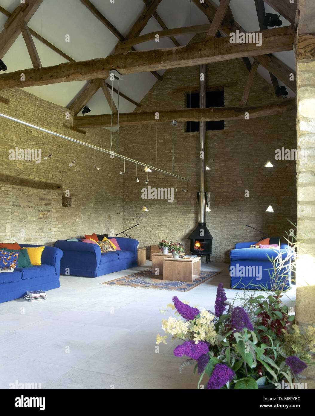 La stanza di seduta in un convertito fienile in pietra con un pavimento piastrellato, esposto a capriate, lit stufa a legna, divani imbottiti e via di illuminazione. Foto Stock