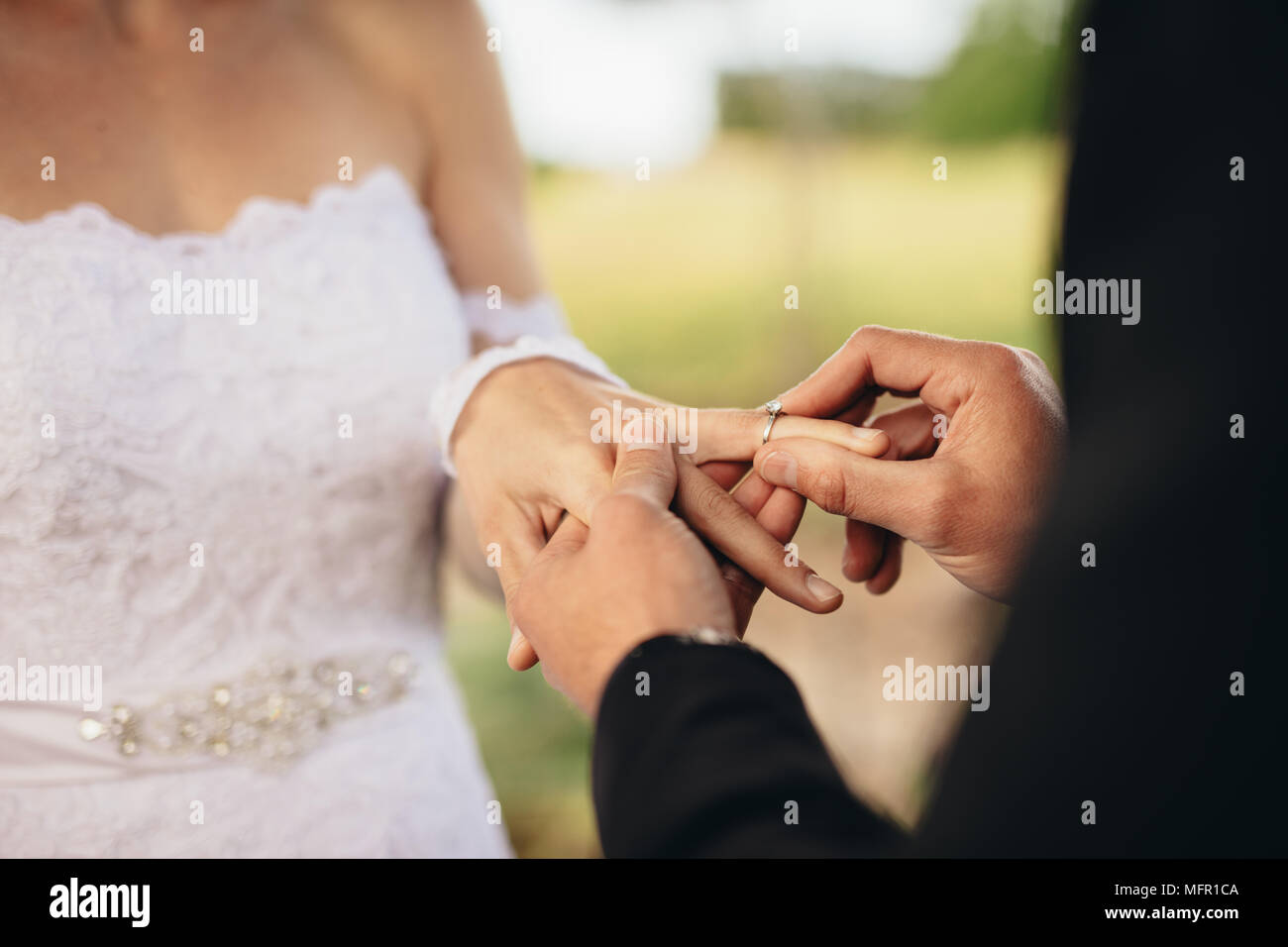 Primo piano della giovane scambiare gli anelli di nozze durante la loro cerimonia di nozze all'esterno. Ritagliato shot di groom mettendo un anello di nozze al dito del b Foto Stock