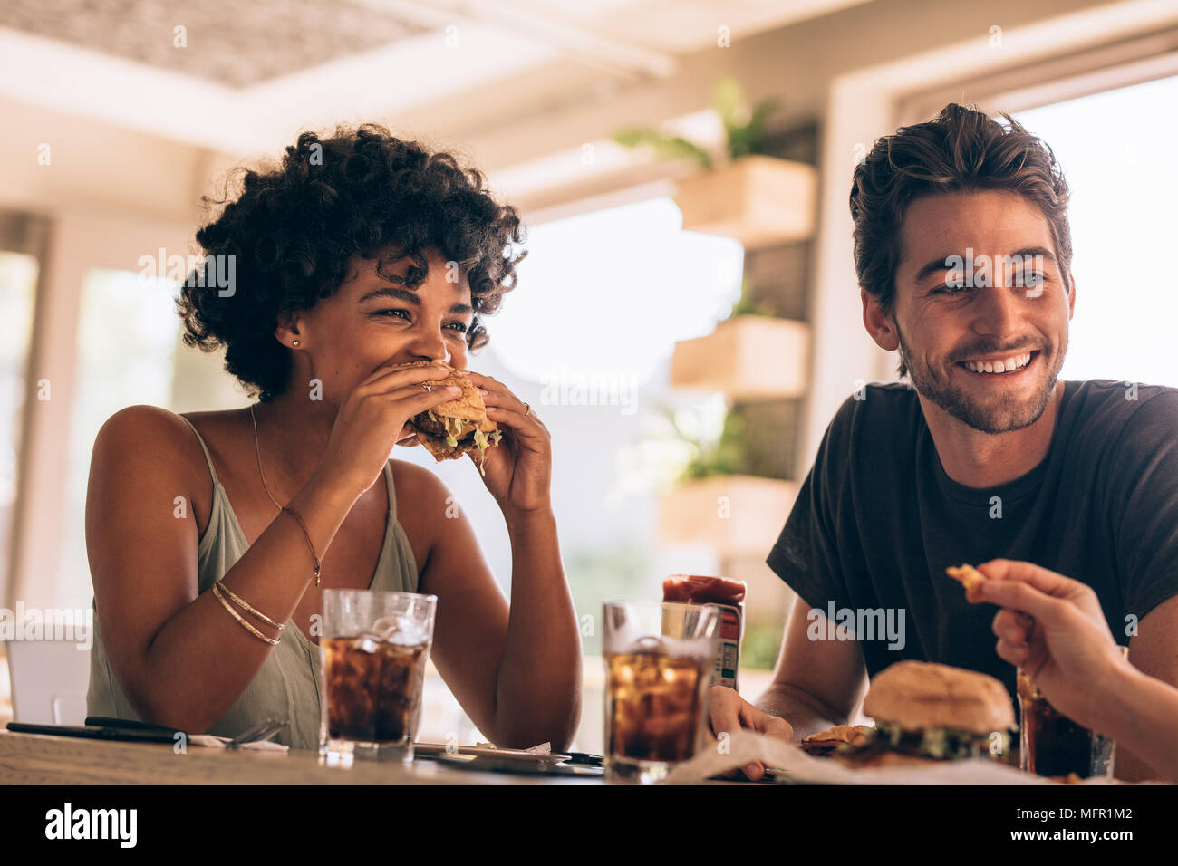 Giovane donna con gli amici a mangiare hamburger al ristorante. Giovani appendere fuori a un caffè chiacchierando e mangiare hamburger. Foto Stock
