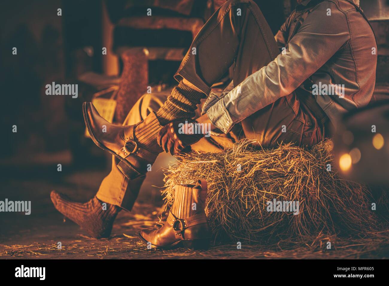 Cowboy nel granaio indossando scarpe mentre posti a sedere sulla pila di  fieno. Agricoltura americana tema Foto stock - Alamy