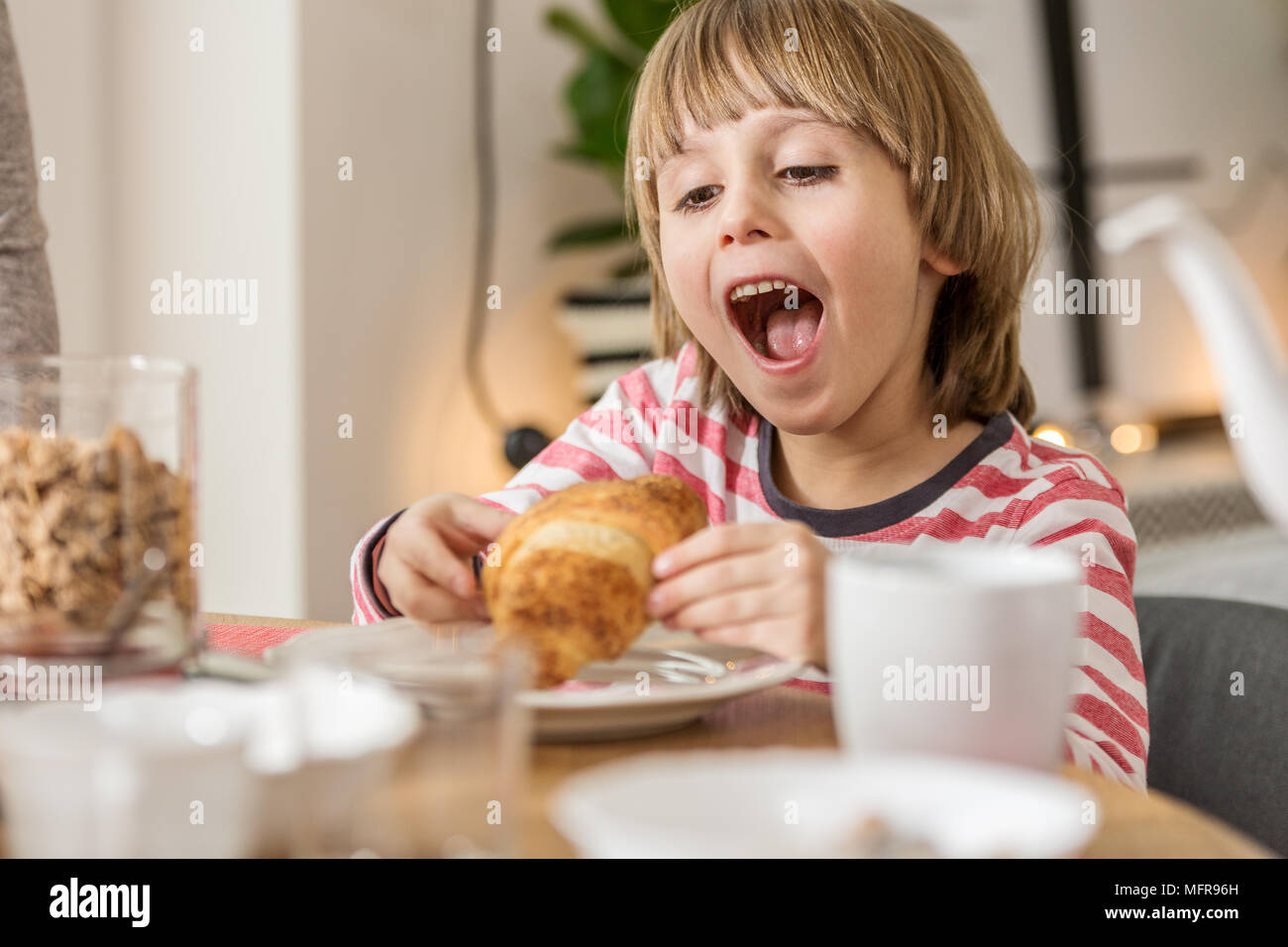 Ragazzo di mangiare un gustoso croissant per la colazione a casa Foto Stock