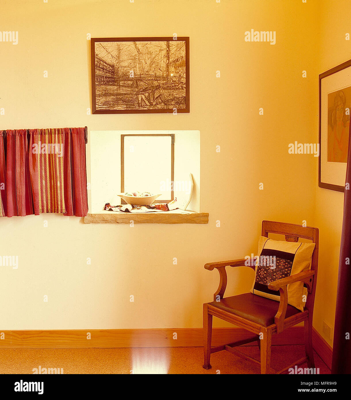 Sedia con braccioli in angolo del paese camera da letto pareti neutre foto incorniciate cuscino piccola finestra tenda ornamenti pianale in legno Foto Stock