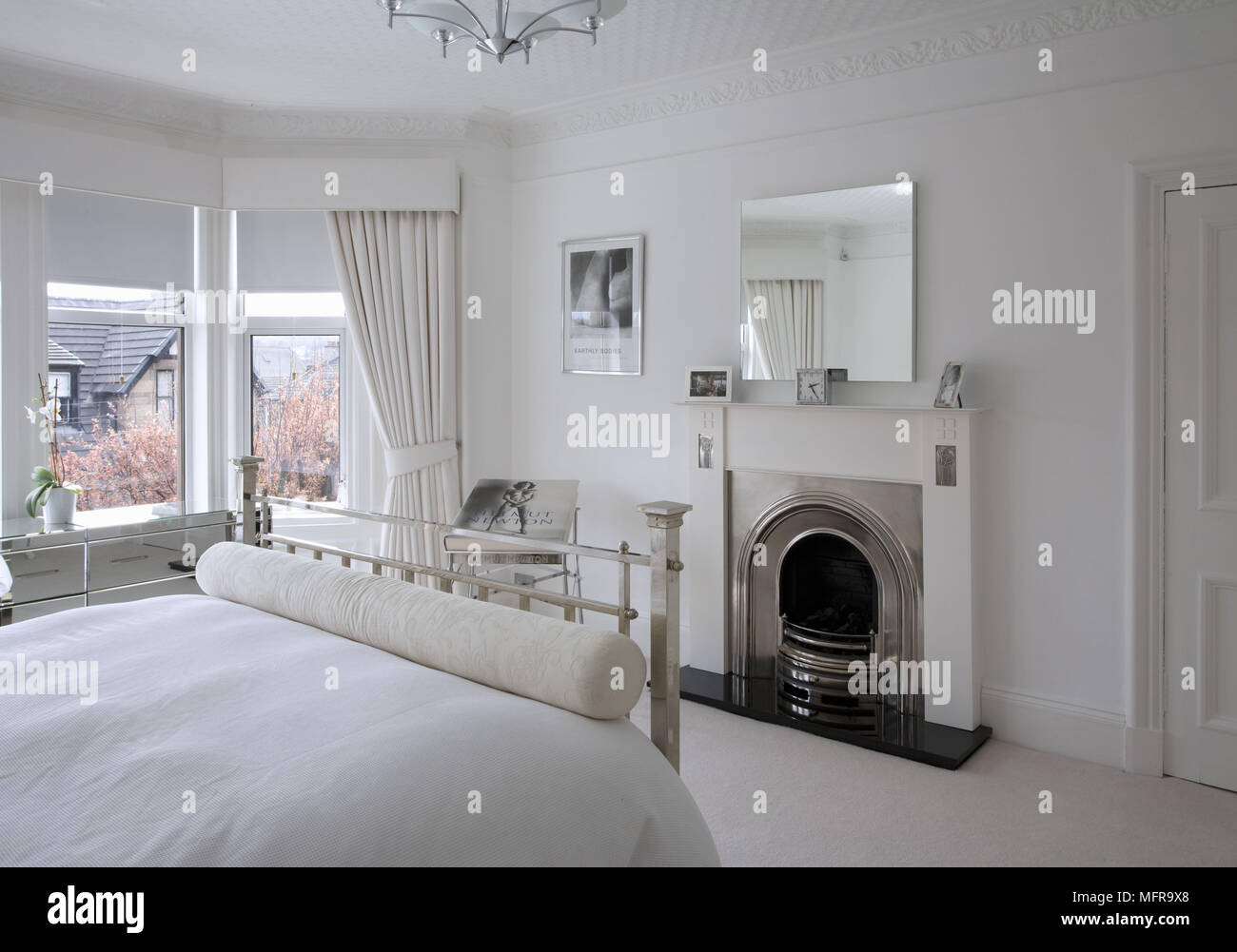 Metallo letto doppia rivolta verso il camino in spaziose bianco in stile tradizionale camera da letto Foto Stock