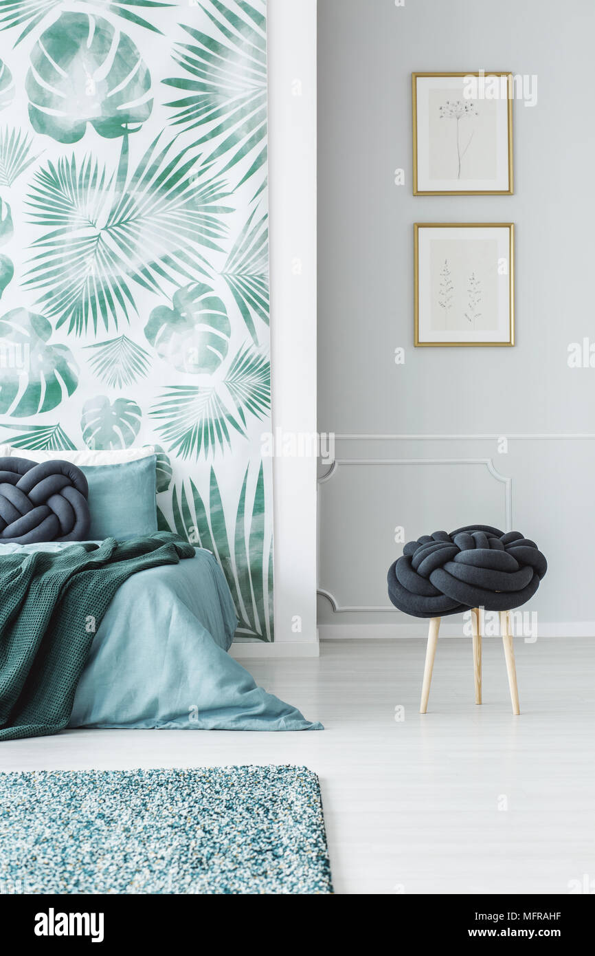 Sgabello accanto al letto di blu in camera da letto interno con carta da  parati di foglie e poster sul muro grigio Foto stock - Alamy