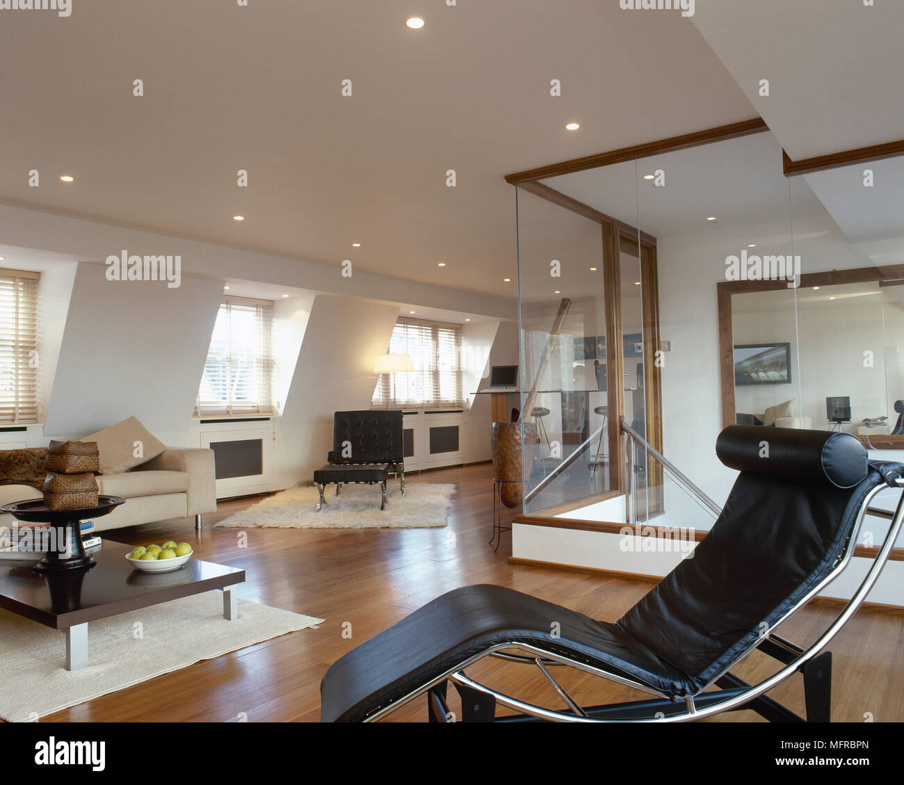 Aprire il piano salotto con pavimento in legno, pelle nera poltrona reclinabile, pareti in vetro e finestre soleggiate. Foto Stock