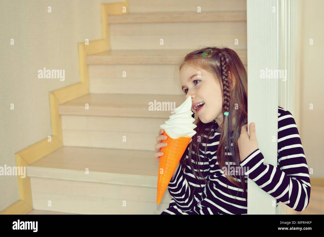 Ragazza bionda, 8 anni, con un gelato, stando in piedi sui gradini, primo piano, ritratto di messa a fuoco selettiva Foto Stock