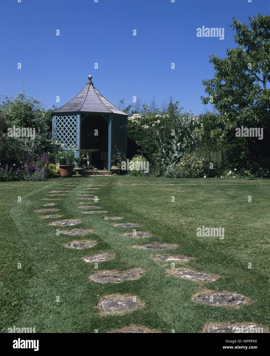 Giardino sul retro con una pietra di un percorso con un gazebo circondato da piante in fiore. Foto Stock