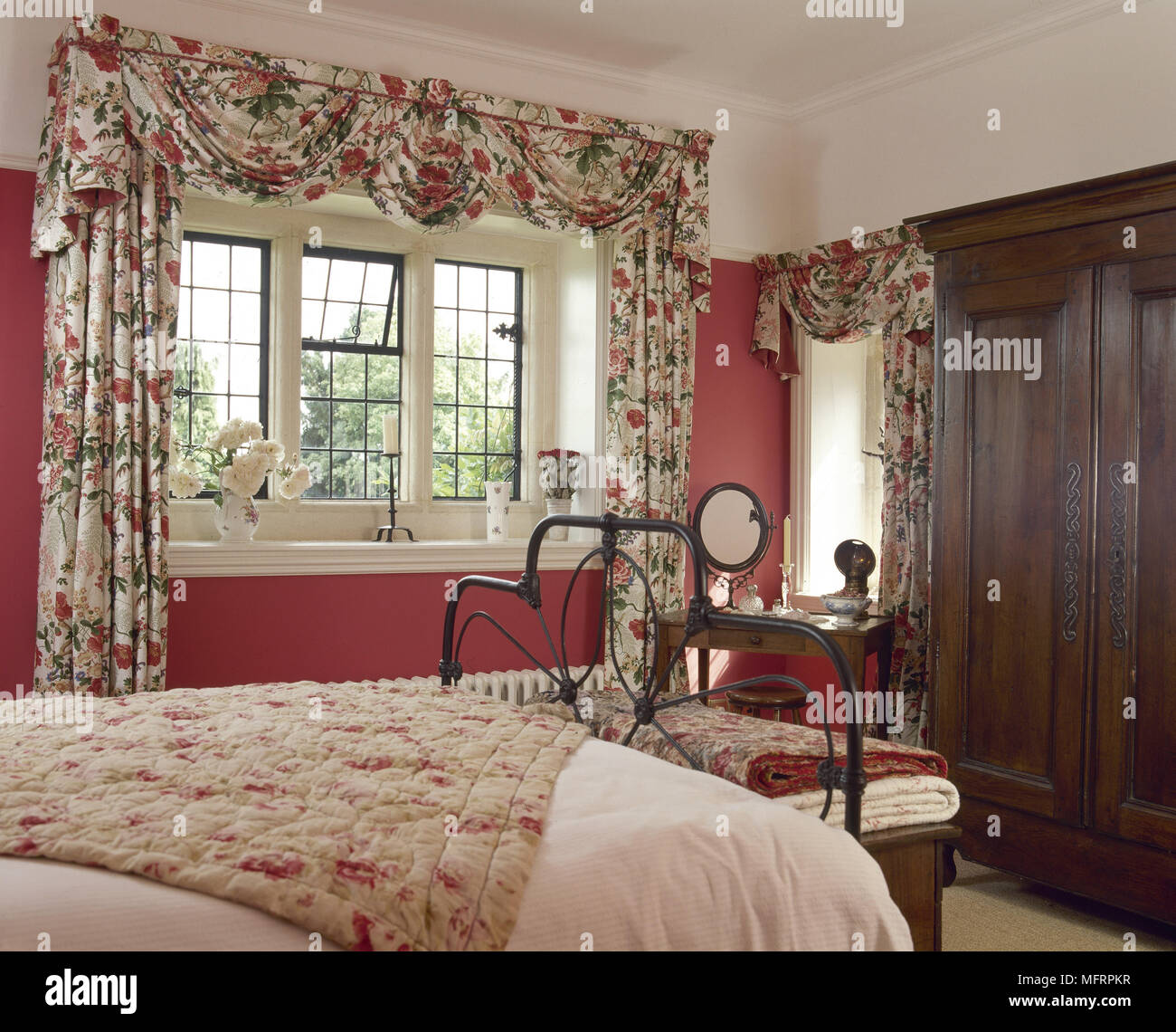 Camera da letto del paese con motivi floreali swag tende, letto di ferro battuto e legno scuro armadio. Foto Stock