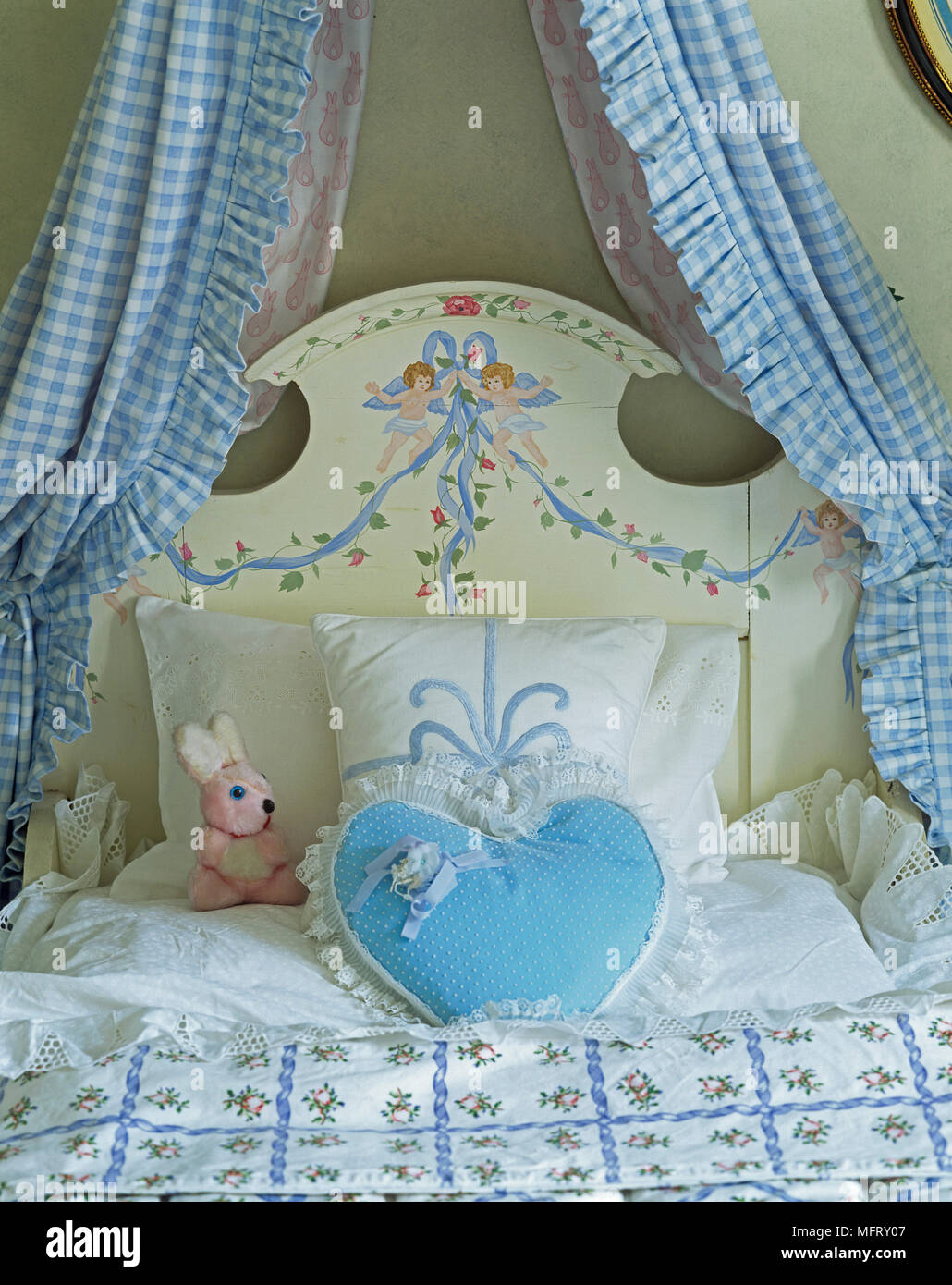 I bambini di legno verniciato letto con blue gingham tendaggi e forma di cuore cuscino Foto Stock