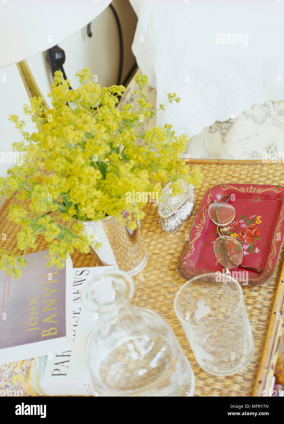 Un dettaglio di una tradizionale camera da letto che mostra un rattan comodino acqua caraffa di vetro fiori Euphorbia; Foto Stock