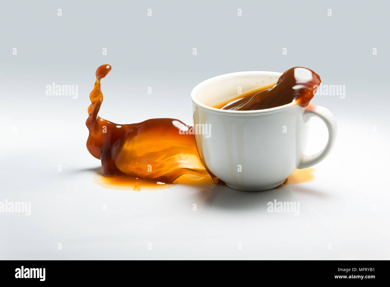 La caduta e la fuoriuscita di una tazza di caffè contro uno sfondo bianco Foto Stock