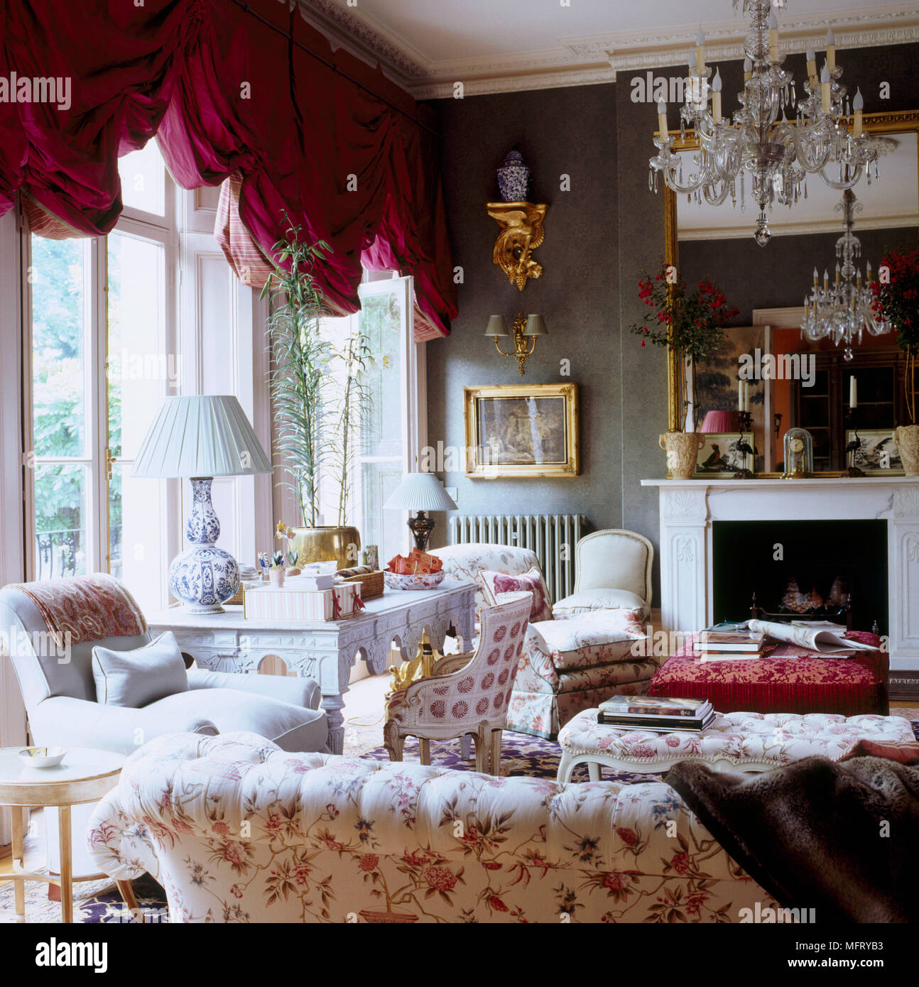 Un grand tradizionale salotto con camino ornato dipinto tavolo divano imbottito rosso tende swag Foto Stock