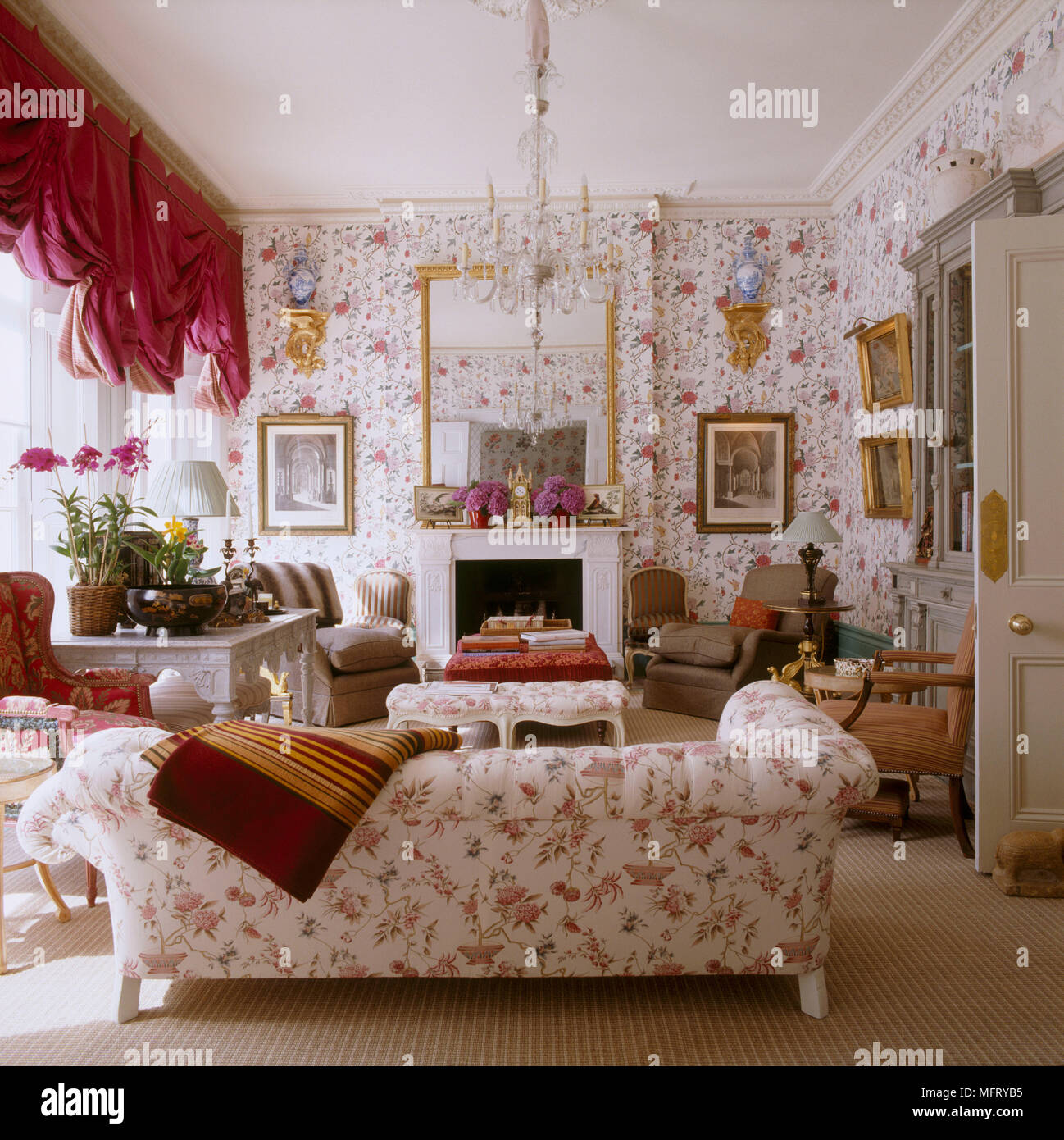 Un grand tradizionale salotto con camino rosso carta da parati floreale divano imbottito swag tende Foto Stock