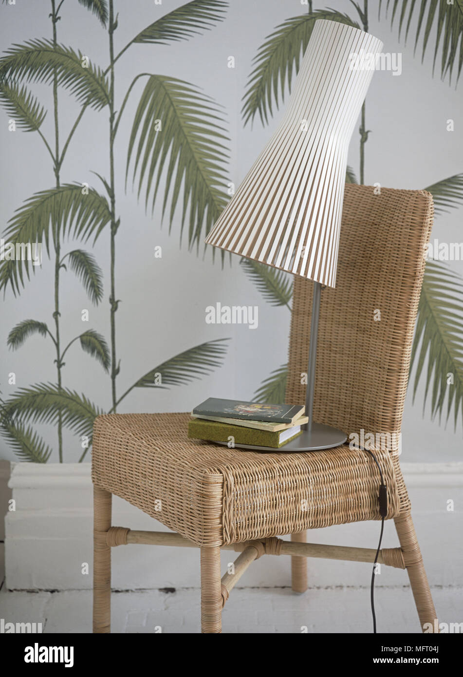 Lampada e libri sulla sedia di vimini contro uno sfondo decorativo Foto Stock