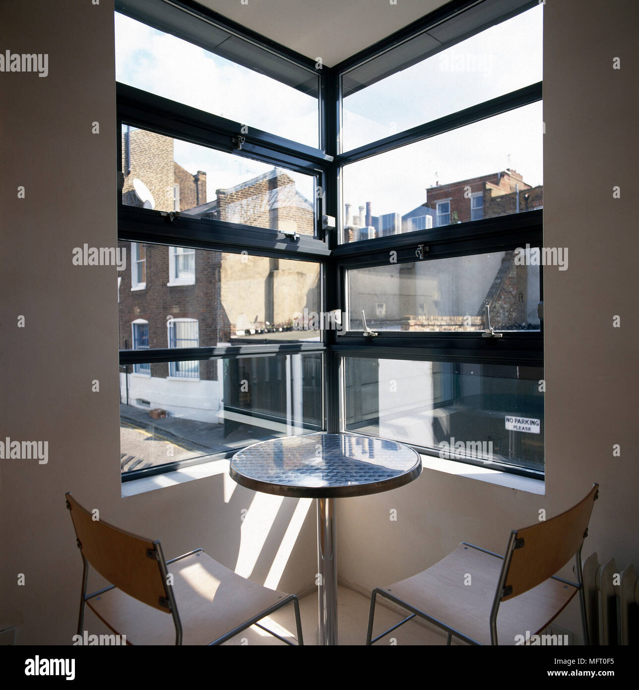 Urban Apartment dettaglio con un piccolo tavolo rotondo e sedie sotto una finestra ad angolo con vista sulla città. Foto Stock