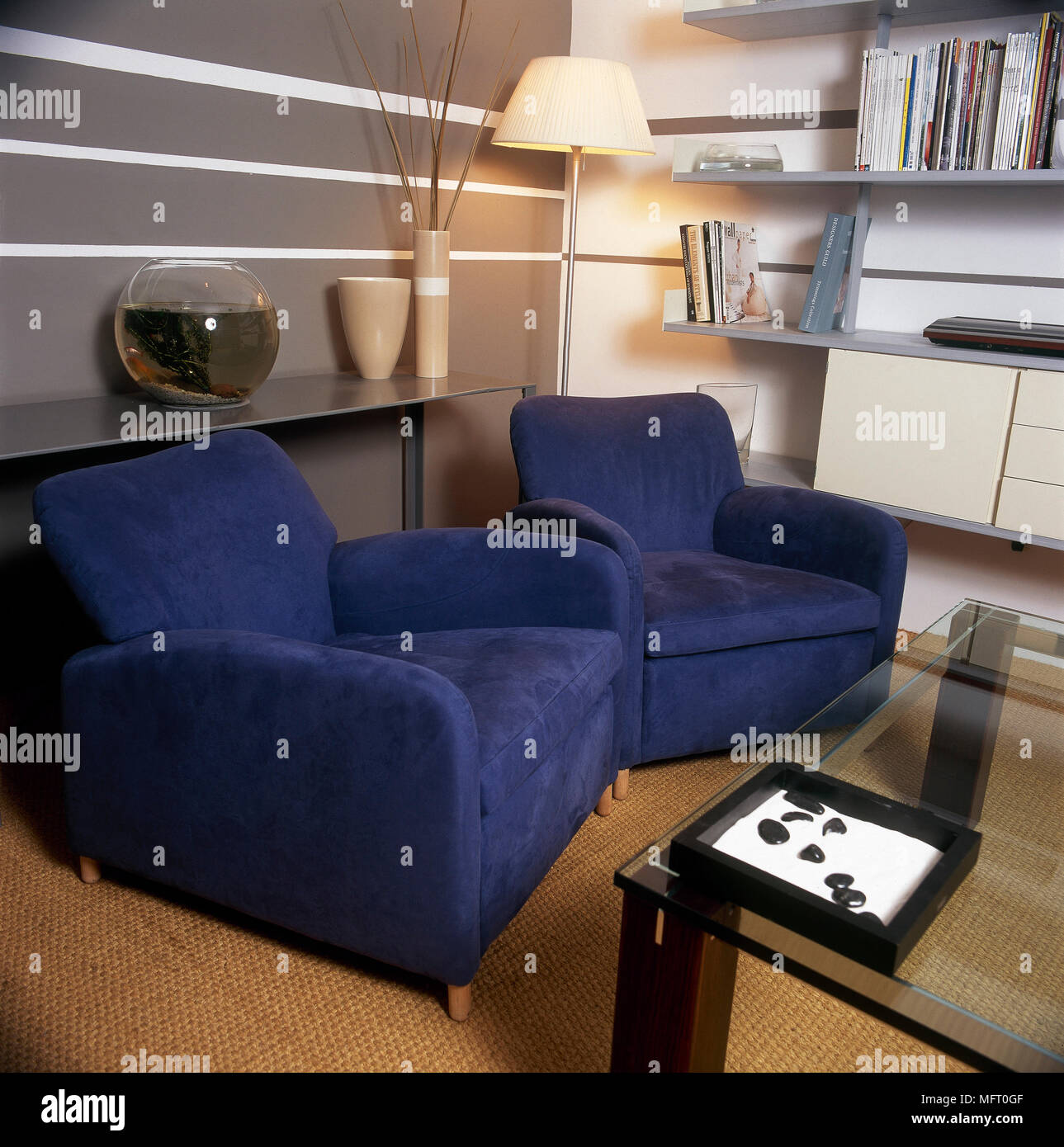 Moderno salotto dettaglio blu con poltrone imbottite, a strisce grigie pareti, top in vetro tavolino da caffè e scaffali aperti. Foto Stock