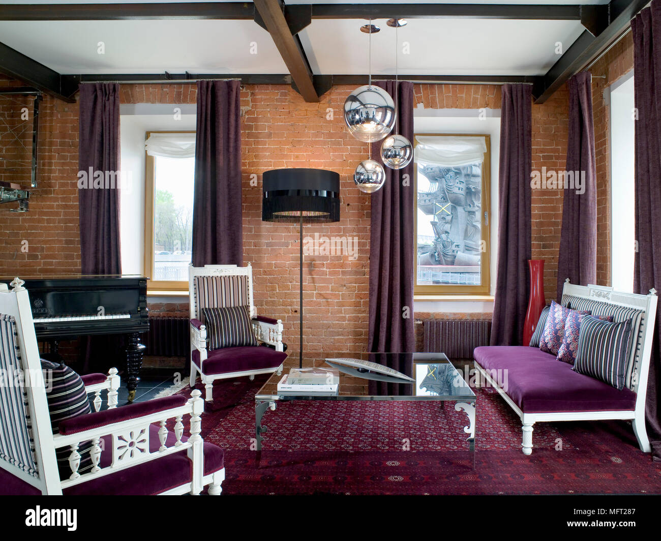 Zona salotto con tappeti color porpora e canapè rivolta verso il ripiano in vetro tavolo da caffè con muri con mattoni a vista e travi in legno a vista Foto Stock