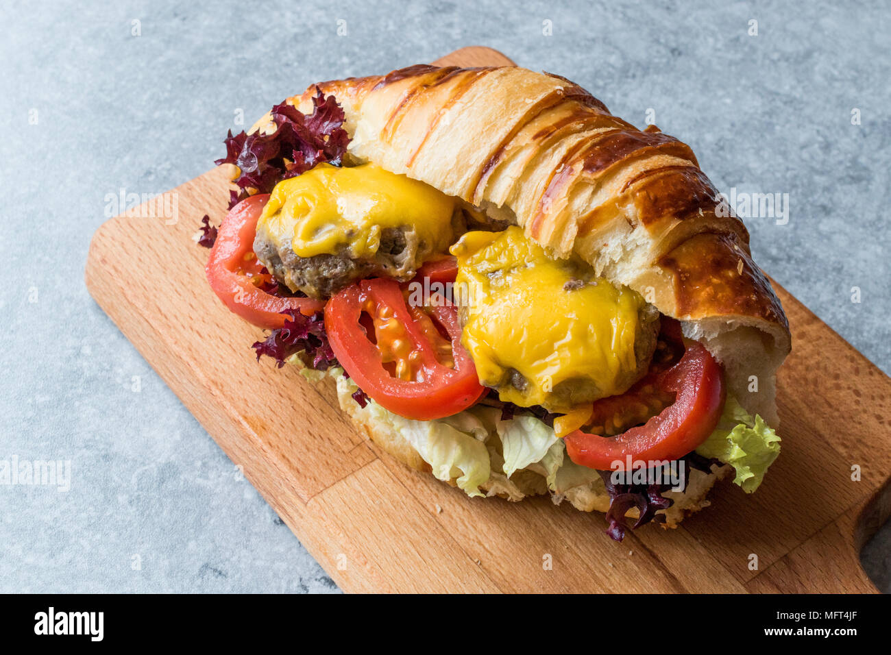 Croissant Burger con polpette di carne, formaggio Cheddar e pomodori. Fast Food. Foto Stock