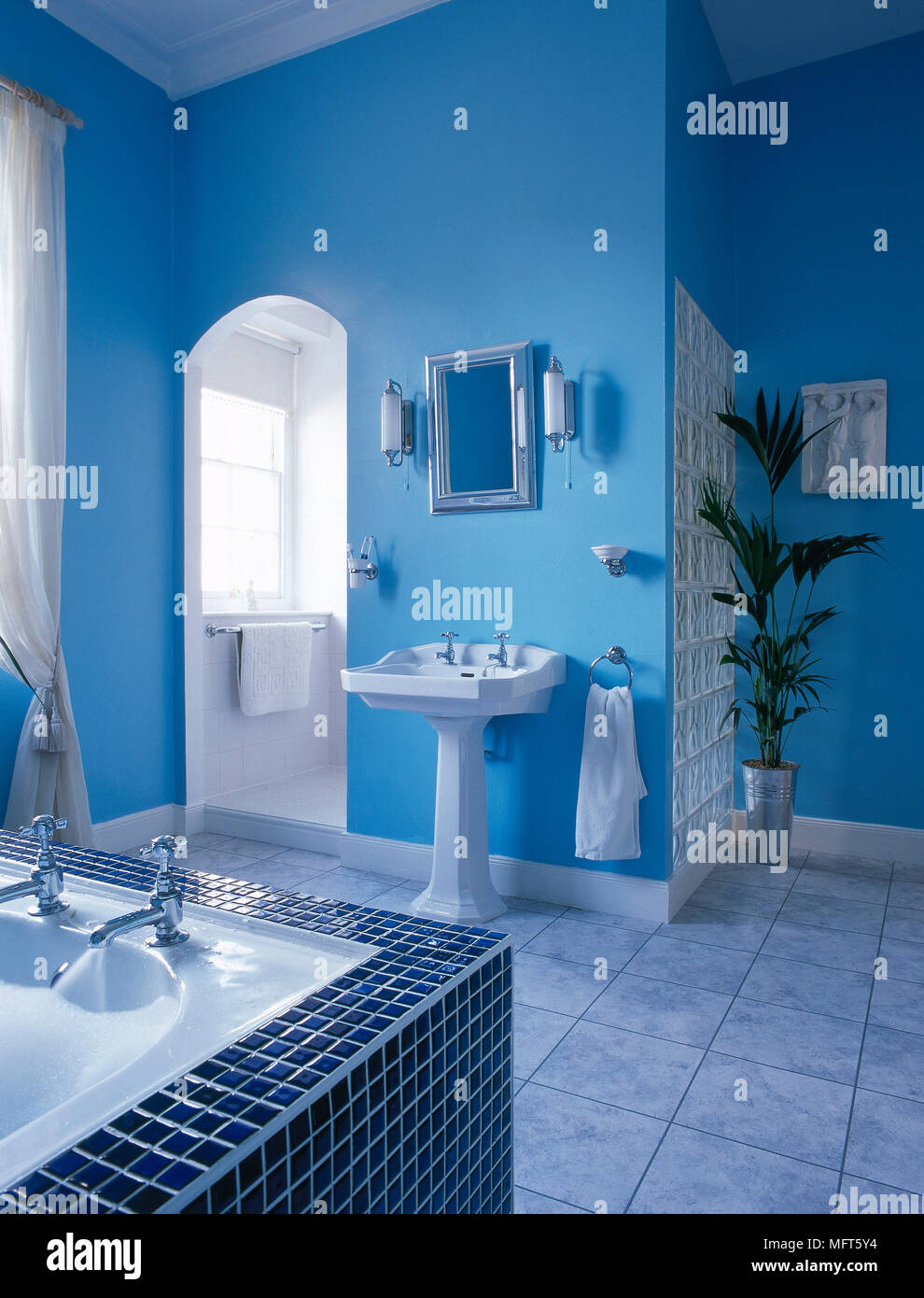 Un bagno moderno con pareti blu, bagno con piastrelle a mosaico surround,  lavabo, blocco di vetro a parete, pavimento piastrellato Foto stock - Alamy