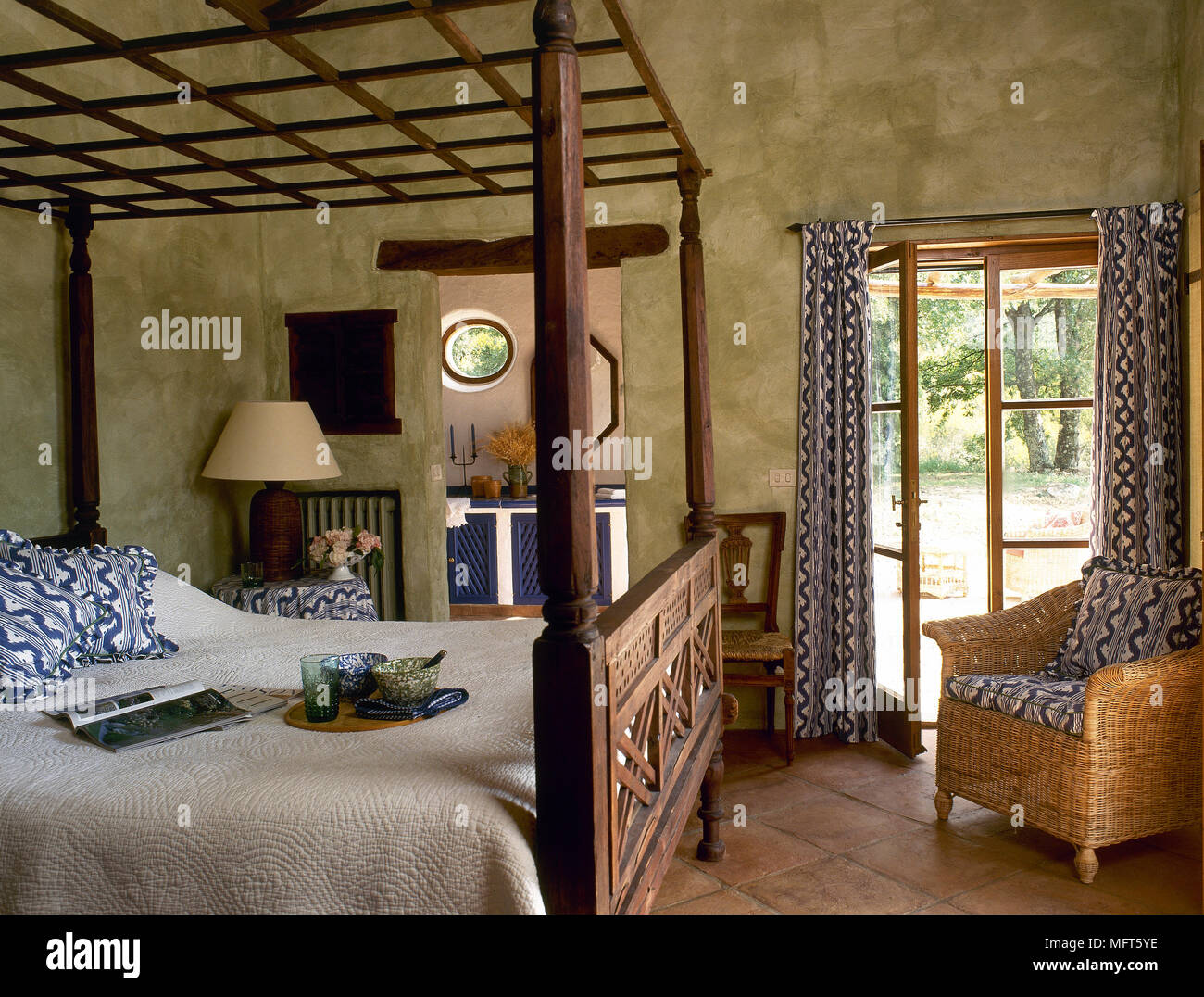 Un rustico, paese con camera da letto in legno intagliato un letto a baldacchino, pattern tende, sedia di vimini, Foto Stock