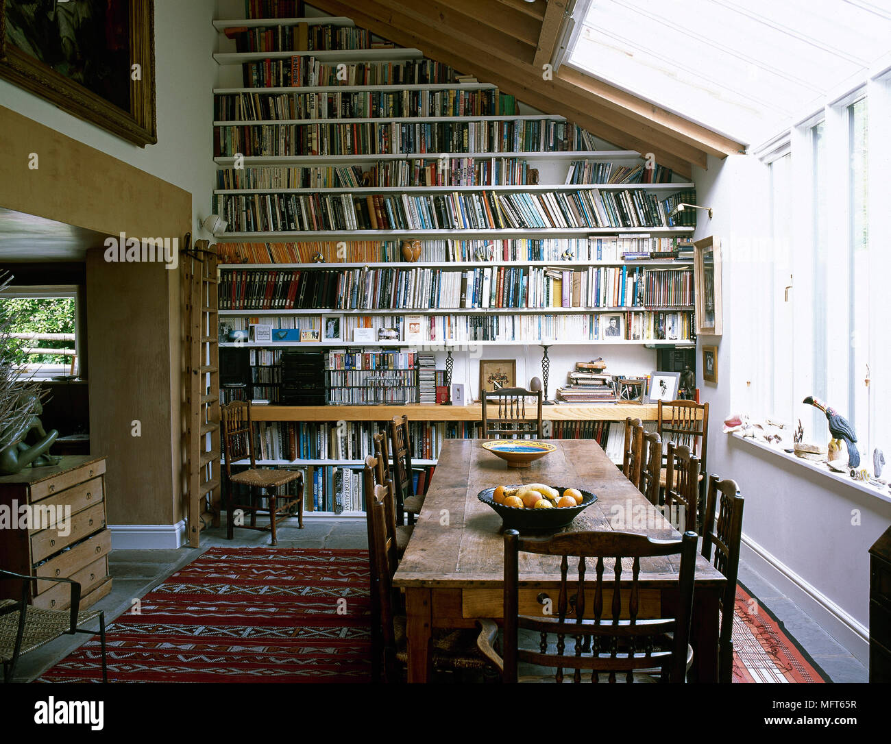 Tavolo in legno e sedie in veranda sala da pranzo con parete riempita con ripiani Foto Stock