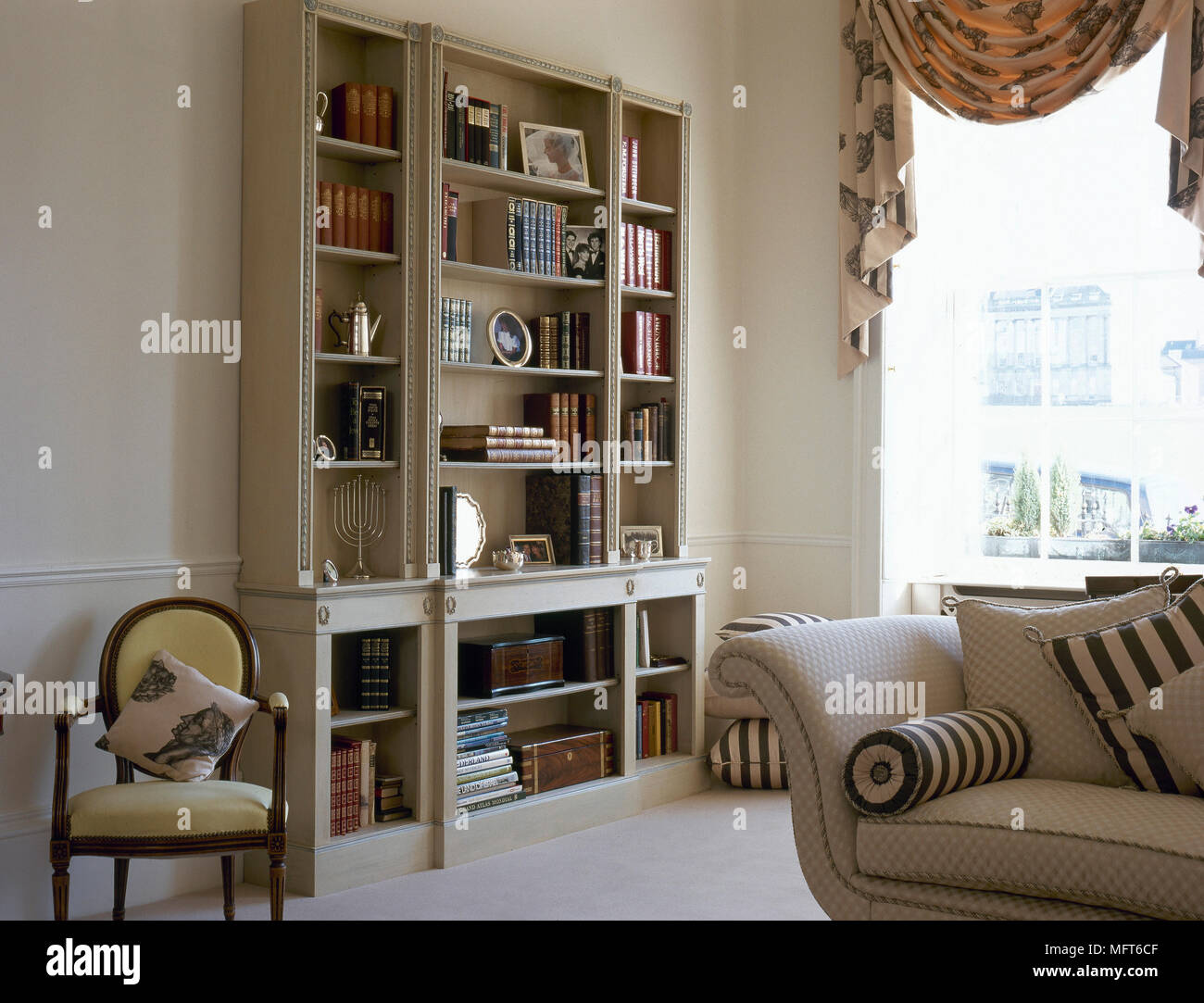 Tradizionale salotto con uno scaffale, divani imbottiti e una finestra piena di sole con swag tende. Foto Stock