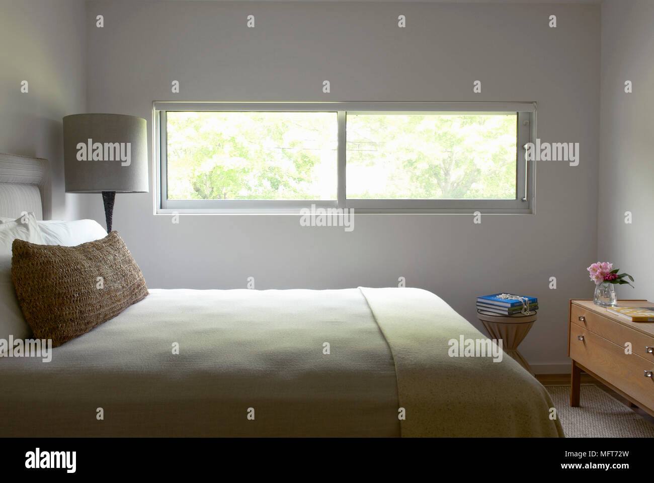 Lampada accanto al letto matrimoniale in camera da letto bianca con finestra stretta Foto Stock