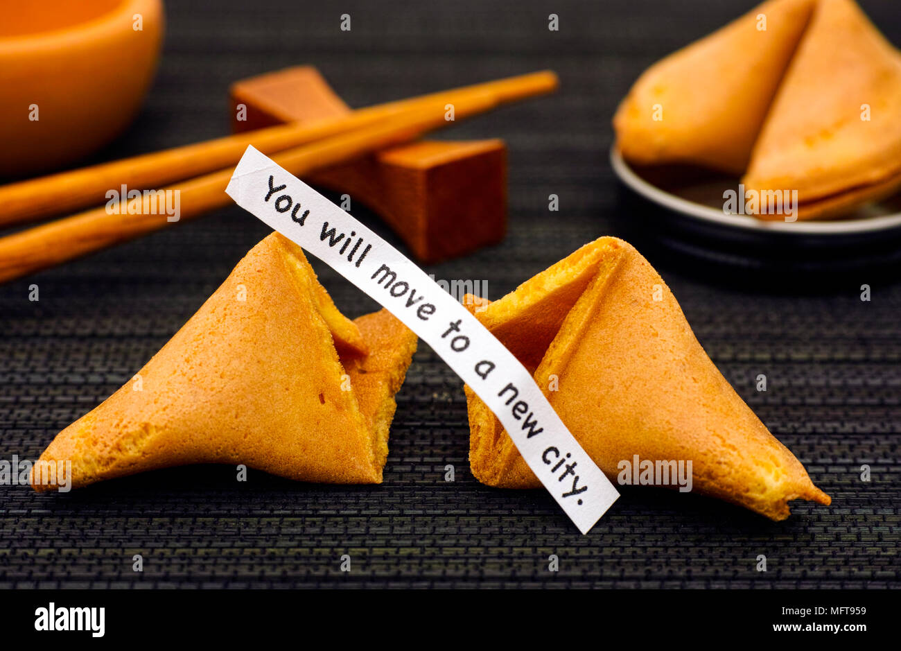 La striscia di carta con la frase che si sposta in una nuova città. da Fortune cookie, un altro biscotto e bacchette sul tovagliolo nero lo sfondo. Foto Stock