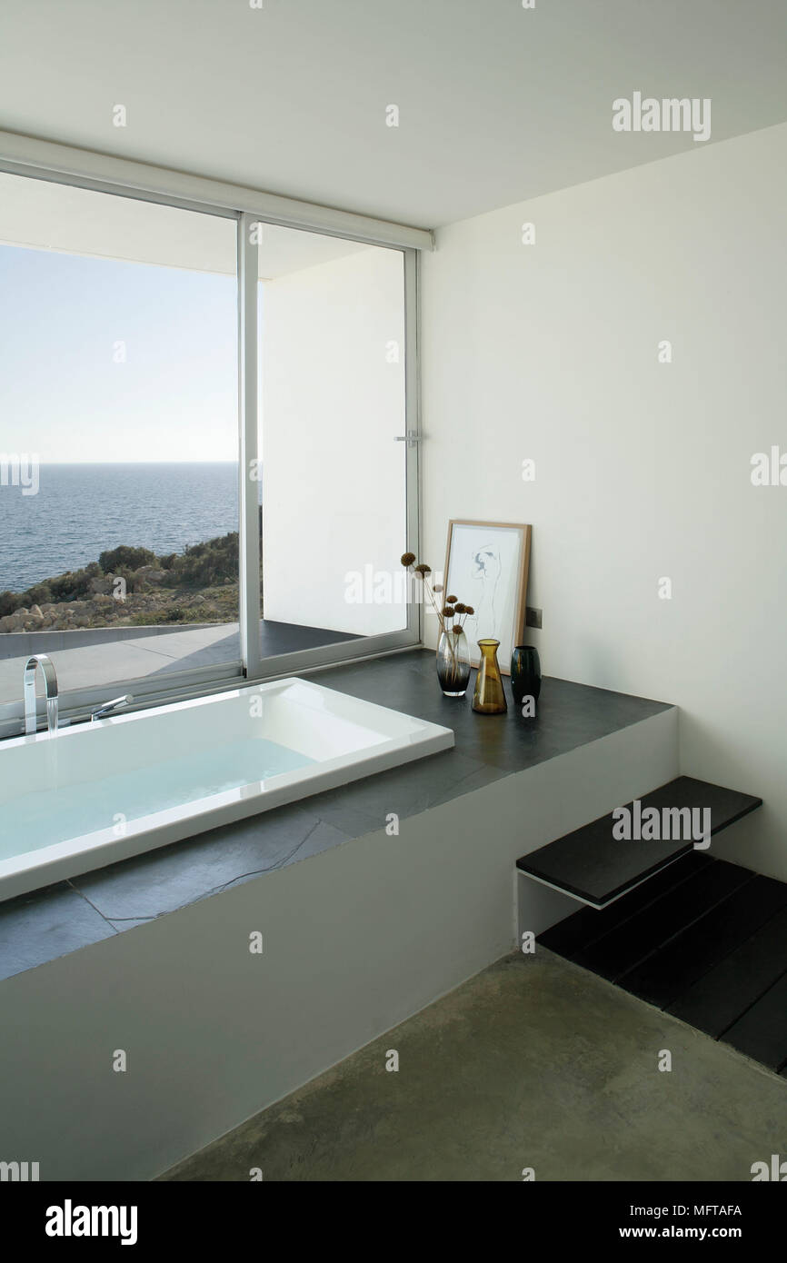 Vasca incassata con surround ardesia in bagno moderno al di sotto della  finestra panoramica con vista oceano Foto stock - Alamy